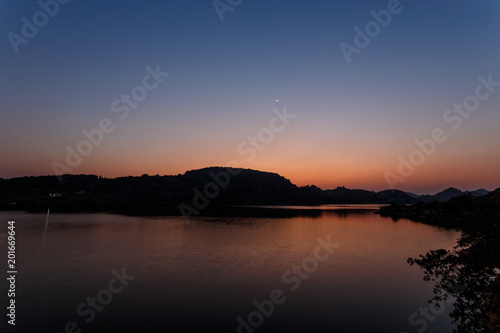 Amazing twilight. The lake is waiting for nightfall. The sun has set by the mountain. Multicolored sky. Silhouettes of mountains. The first stars are lit. New moon.India. Hampi. Magical lake. © mishamif