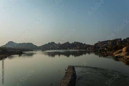 Lake in Hampi. Reflections in the water of the cave city and rocks in the early morning in the Indian state of Karnataka.A hazy haze can be seen on the horizon. Landscape panorama.Amazing view.