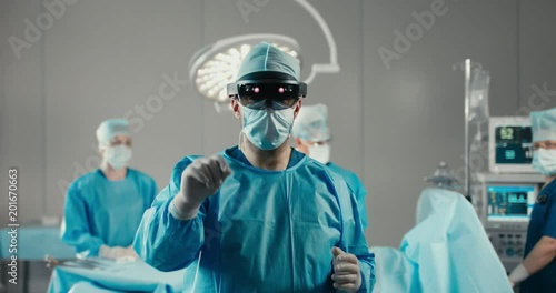 Front view half portrait of surgeon using augmented reality holographic hololens headset, preparing for operation in modern operation theater. 4K UHD 60 FPS SLO MO photo