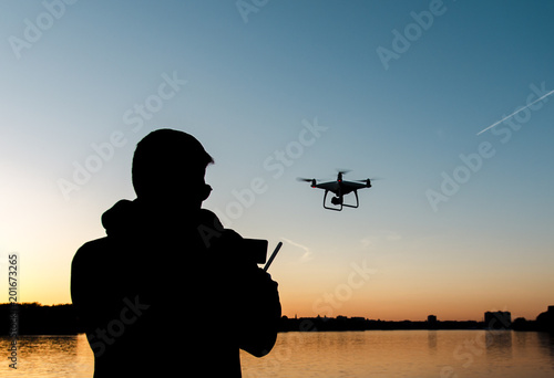 Silhouette of man flying drone by the river at sunset 