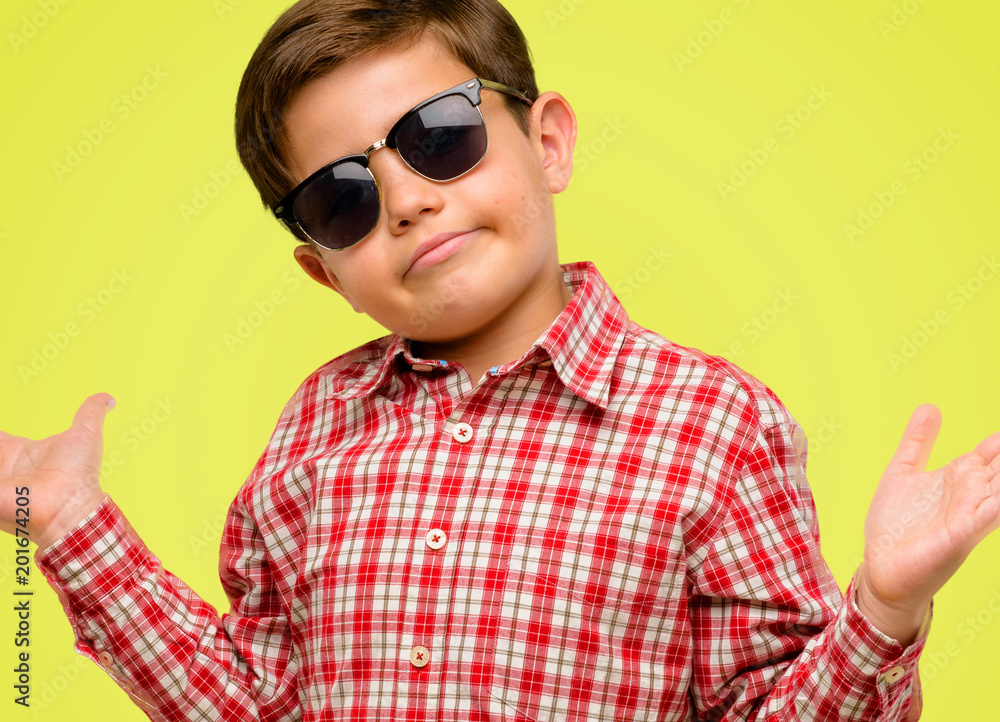 Handsome toddler child with green eyes doubt expression, confuse and wonder concept, uncertain future over yellow background Handsome toddler child with green eyes doubt expression, confuse and wonder concept, uncertain future over yellow background