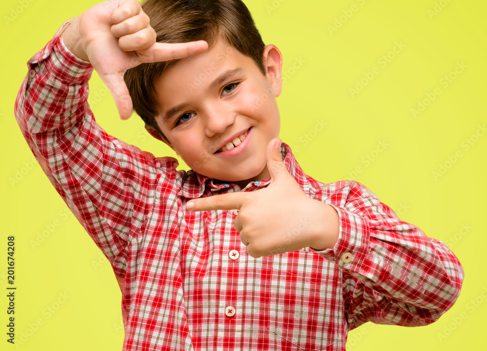 Handsome toddler child with green eyes confident and happy showing hands to camera, composing and framing gesture over yellow background Handsome toddler child with green eyes confident and happy showing hands to camera, composing and framing gesture over yellow background