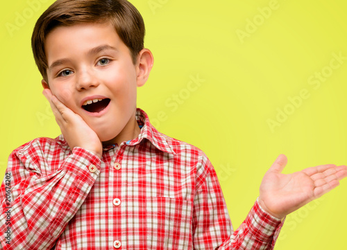 Handsome toddler child with green eyes holding something in empty hand over yellow background