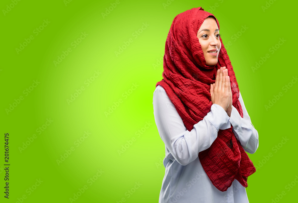 Young arab woman wearing hijab with hands together in praying gesture, expressing hope and please concept Young arab woman wearing hijab with hands together in praying gesture, expressing hope and please concept
