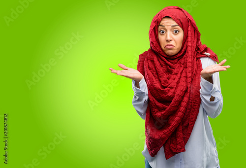 Young arab woman wearing hijab doubt expression  confuse and wonder concept  uncertain future shrugging shoulders