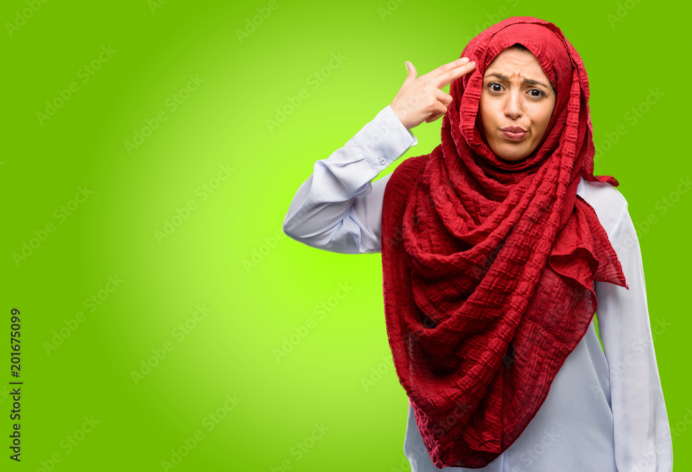 Portrait of woman in hijab making suicide gesture against green background Portrait of woman in hijab making suicide gesture against green background