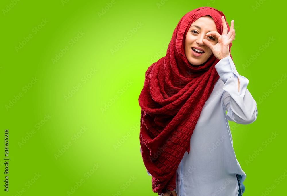 Young arab woman wearing hijab looking at camera through her fingers in ok gesture. Imitating binoculars, beautiful eyes and smile Young arab woman wearing hijab looking at camera through her fingers in ok gesture. Imitating binoculars, beautiful eyes and smile