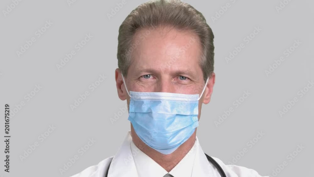 Close-up portrait of serious man doctor in white surgical mask. Mature friendly caucasian smiling physician, grey isolated background. Close-up portrait of serious man doctor in white surgical mask. Mature friendly caucasian smiling physician, grey isolated background.