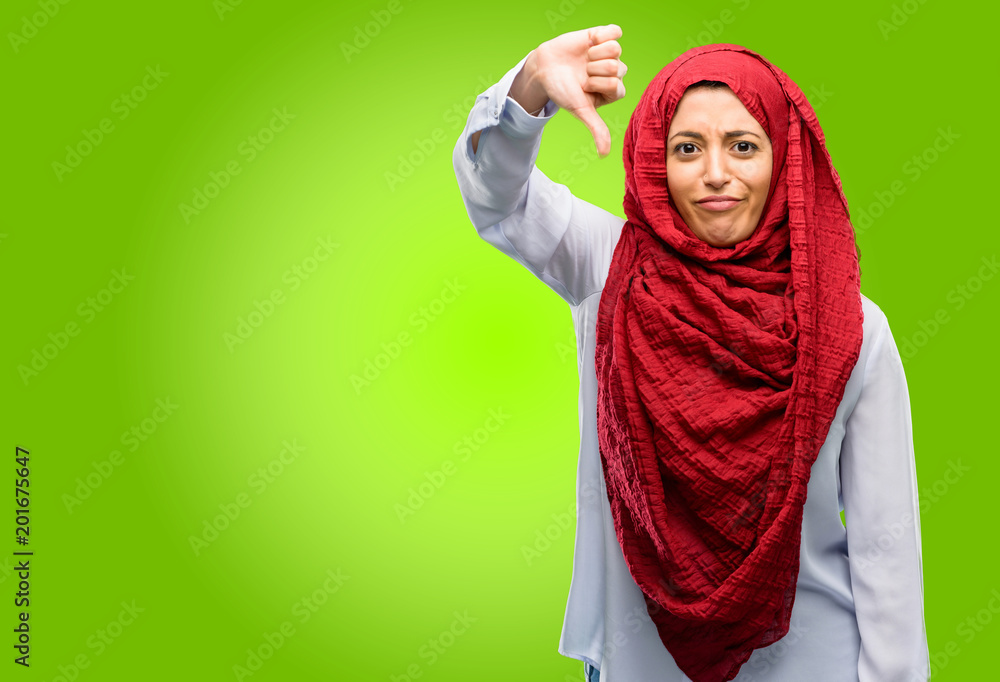 Young arab woman wearing hijab showing thumbs down unhappy sign of dislike, negative expression and disapproval Young arab woman wearing hijab showing thumbs down unhappy sign of dislike, negative expression and disapproval