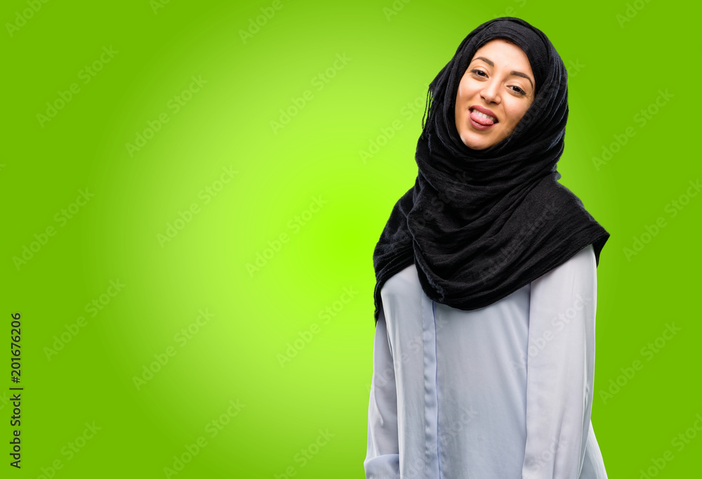 Young arab woman wearing hijab sticking out tongue at camera at sign of disobedience, protest and disrespect Young arab woman wearing hijab sticking out tongue at camera at sign of disobedience, protest and disrespect