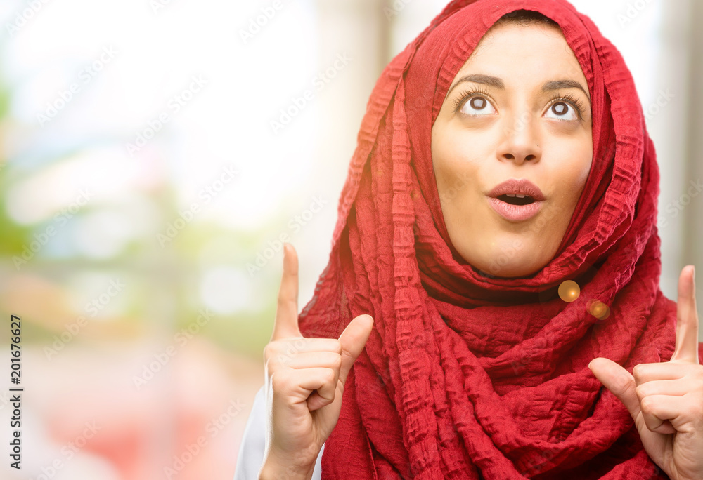 Young arab woman wearing hijab happy and surprised cheering expressing wow gesture pointing up Young arab woman wearing hijab happy and surprised cheering expressing wow gesture pointing up