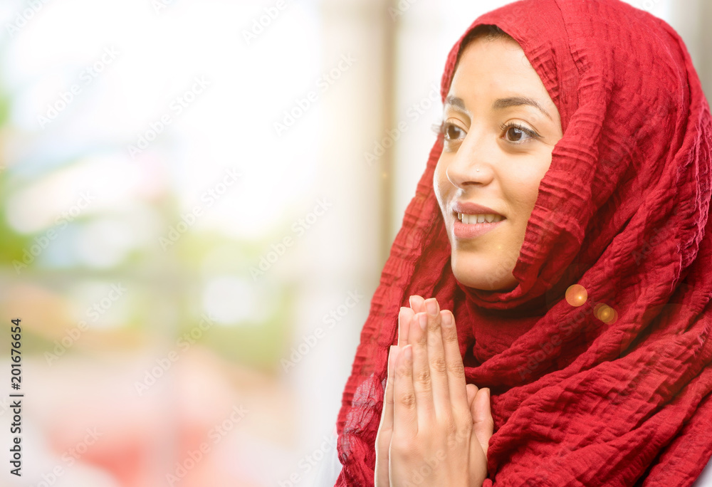 Young arab woman wearing hijab with hands together in praying gesture, expressing hope and please concept Young arab woman wearing hijab with hands together in praying gesture, expressing hope and please concept