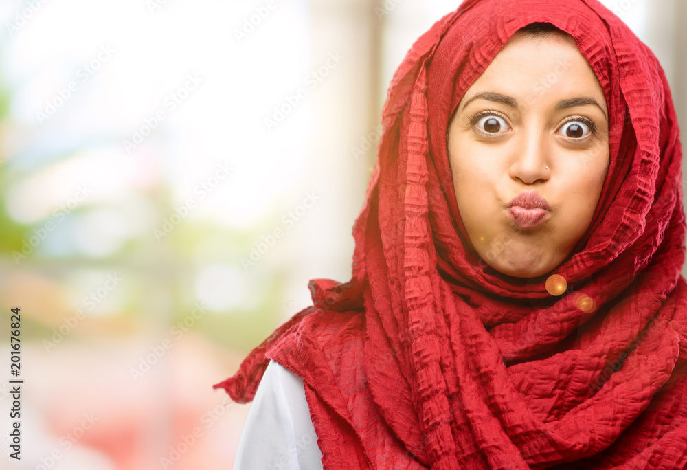 Young arab woman wearing hijab puffing out cheeks, having fun making funny face Young arab woman wearing hijab puffing out cheeks, having fun making funny face