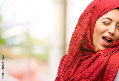 Young arab woman wearing hijab blinking eyes with happy gesture