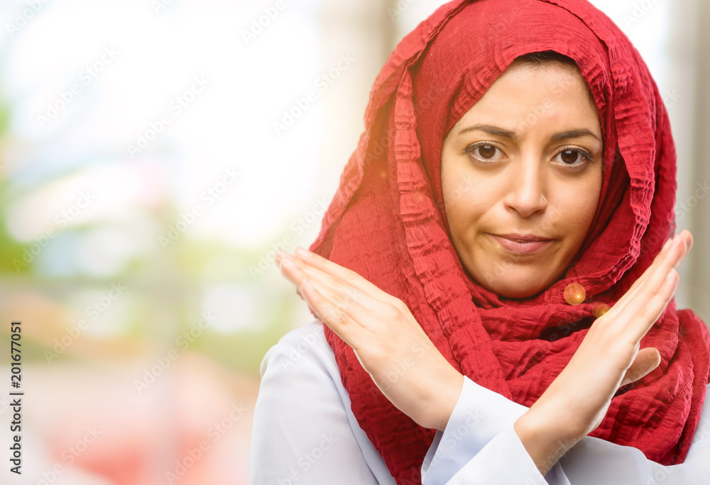 Young arab woman wearing hijab annoyed with bad attitude making stop sign crossing hands, saying no, expressing security, defense or restriction Young arab woman wearing hijab annoyed with bad attitude making stop sign crossing hands, saying no, expressing security, defense or restriction