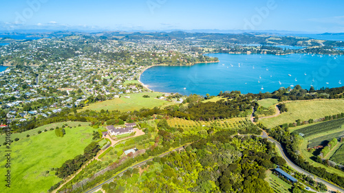 Aerial view on a vineyard on the shore of sunny harbour with residential suburbs on the background. Waiheke Island, Auckland, New Zealand. © Dmitri