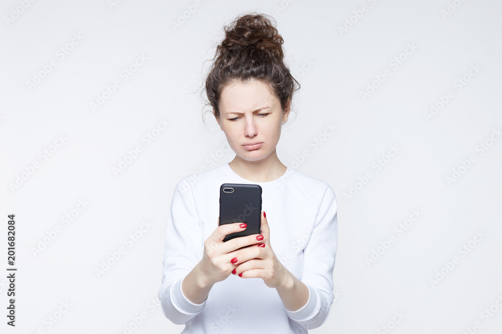 Unhappy American student feeling uncomfortable and ashamed, looking down at screen of phone with sad expression while having troubles at college. Portrait of sad young pretty female with no motivation Unhappy American student feeling uncomfortable and ashamed, looking down at screen of phone with sad expression while having troubles at college. Portrait of sad young pretty female with no motivation
