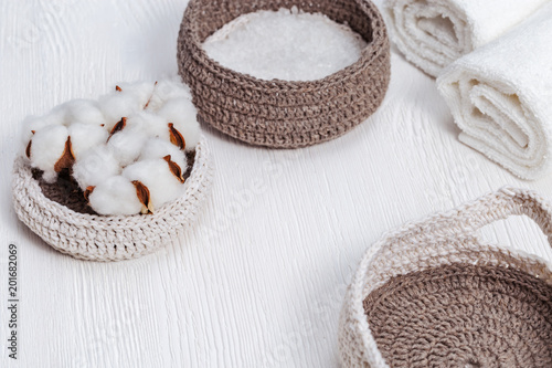 Spa concept. Flower of cotton plant, bath salt in knitted box, white rolled towel on wooden background with copy space.