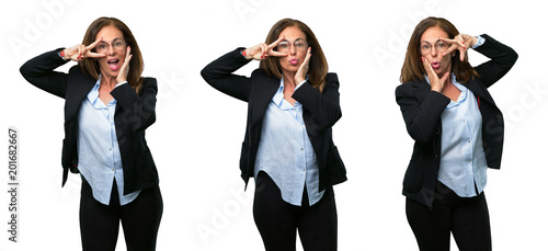 Middle age business woman looking at camera through her fingers in victory gesture winking the eye and blowing a kiss over white background