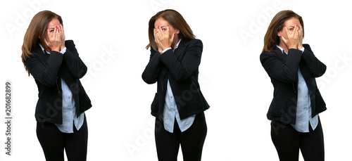 Middle age business woman smiling having shy look peeking through her fingers  covering face with hands looking confusedly broadly over white background