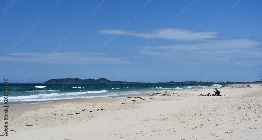 Byron beach in sunny afternoon with blue sky in Byron Bay, Australia. People relaxing on the beach.