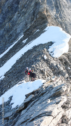 mountain guide leading two male clients to a rocky ridge and onwards to a high alpine summit photo