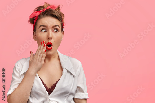Wallpaper Mural Amazed pinup girl looks with stunned expression, keeps mouth rounded, has red manicure, looks with shock away at blank copy space, isolated over pink background. Pretty woman has retro style Torontodigital.ca