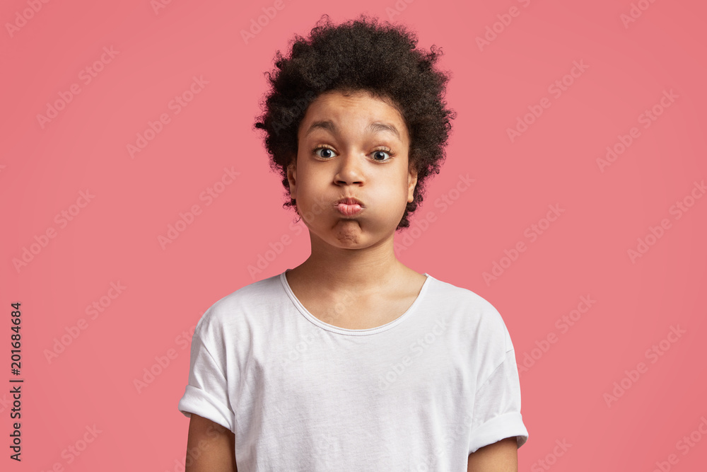 Portrait of small mixed race male kid blows cheeks and puffs breath, has  attractive look and