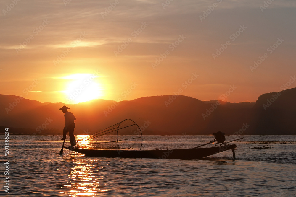 Fisherman silhouette at the sunset on the Inle Lake, Myanmar (Fishermen on the Inle Lake use traditional one-leg rowing technique)