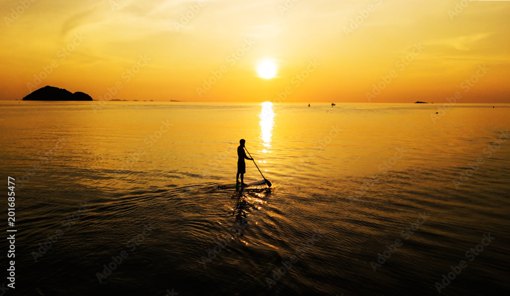 Aerial: Sunset silhouette of a person standing up at paddle board on vacation in Thailand