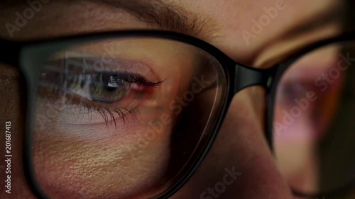 Woman in glasses looking on the monitor and surfing Internet. The monitor screen is reflected in the glasses