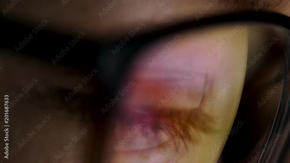 Woman in glasses looking on the monitor and surfing Internet. The monitor screen is reflected in the glasses Woman in glasses looking on the monitor and surfing Internet. The monitor screen is reflected in the glasses
