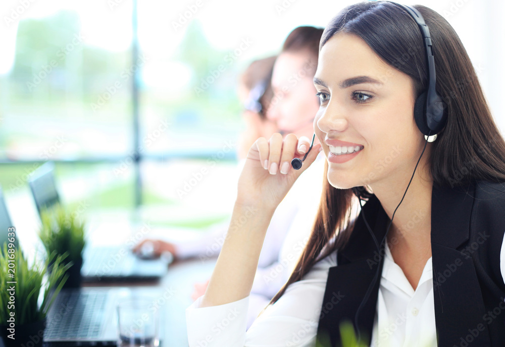 Portrait of smiling female customer service agent wearing headset with colleagues working in background at office. Portrait of smiling female customer service agent wearing headset with colleagues working in background at office.