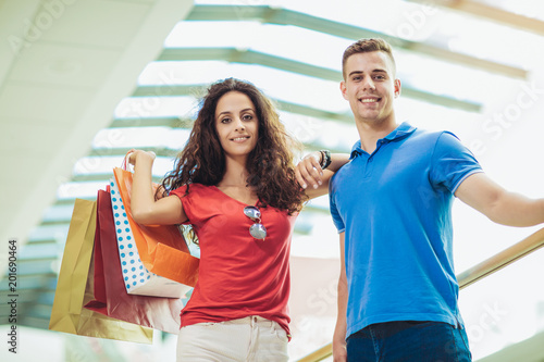 Happy beautiful young couple holding shopping bags and smiling while doing shopping in mall