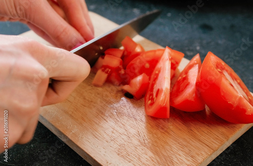 Closeup woman's hands cutting tomatoes on a wood board.