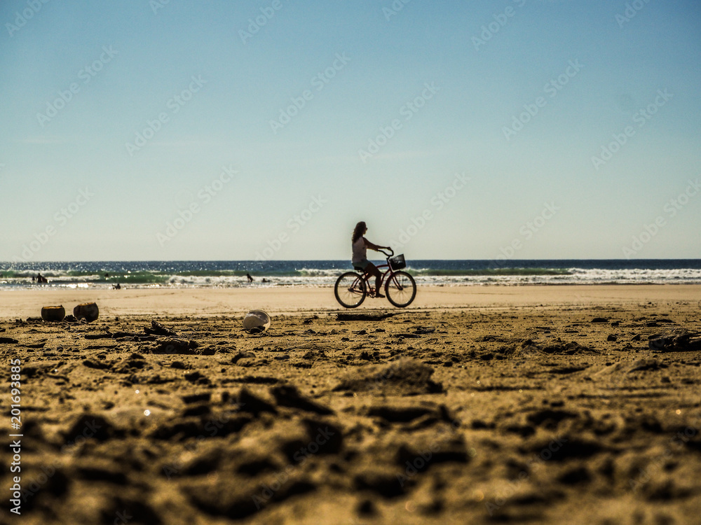 Fototapeta premium woman riding bicycle on a wide beach close to the ocean during sunset