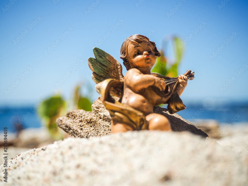Obraz premium young Guardian Angel sitting in the sand on the beach and playing ukulele while saving the world