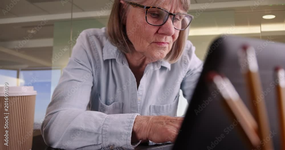 Close-up of senior woman typing on laptop working in corporate workplace, Portrait of older woman using portable computer in modern office space setting, 4k Close-up of senior woman typing on laptop working in corporate workplace, Portrait of older woman using portable computer in modern office space setting, 4k