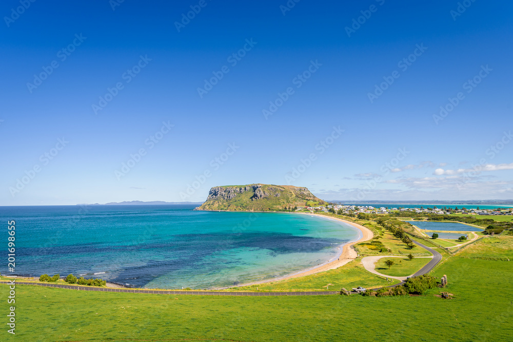 Stunning view point to big old volcanic rock mountain top called The Nut with blue turquoise water beach bay and green grass lands on warm sunny clear sky day, Stanley, North-West, Tasmania, Australia