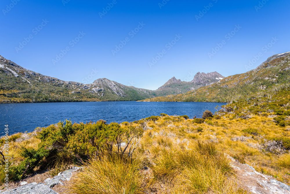 Pretty view to great deep blue mountain lake and green orange shore jungle forest bush land on warm sunny clear sky hiking wilderness day, Dove Lake, Cradle Mountain National Park, Tasmania, Australia
