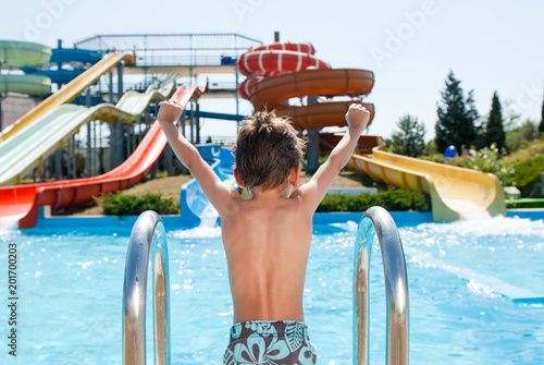 healthy happy little kid near blue swimming pool in water park with water tube slides in summer photo