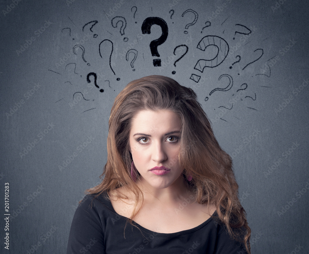 A pretty teenage girl standing confused in front of grey wall background with drawn question marks concept. A pretty teenage girl standing confused in front of grey wall background with drawn question marks concept.