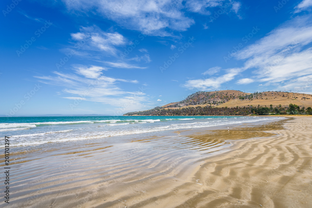 Beautyful view to small paradise like sandy waves beach with turquoise blue water and shore mussels coast stripes mountains on warm sunny clear sky day, Seven Miles Beach, Hobart, Tasmania, Australia