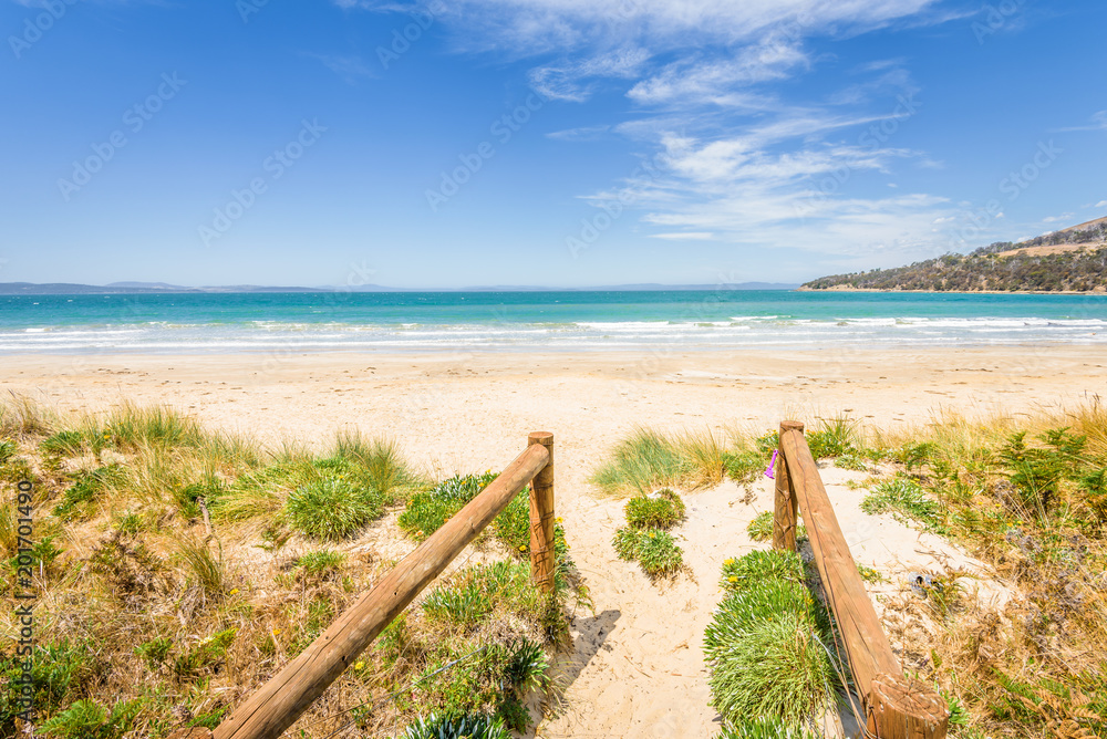 Beautyful view to small paradise like sandy waves beach with turquoise blue water and shore mussels coast stripes mountains on warm sunny clear sky day, Seven Miles Beach, Hobart, Tasmania, Australia