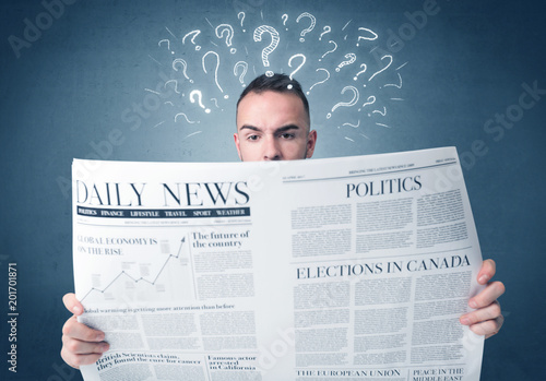 Young confused businessman reading daily newspaper with question marks above his head