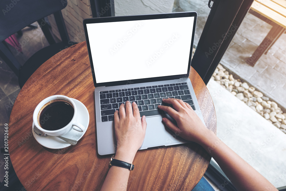 Top view mockup image of a woman using and typing on laptop with blank white desktop screen on wooden table in cafe