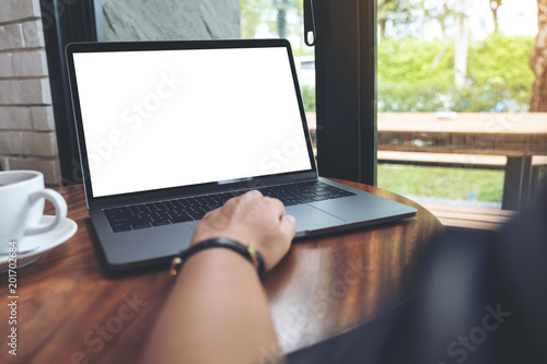 Mockup image of a woman using and typing on laptop with blank white desktop screen on wooden table in cafe