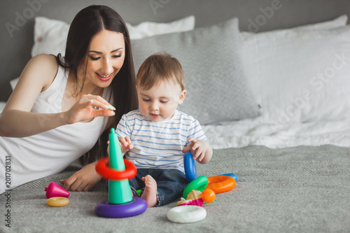 Young pretty mother playing with her little son. Cheerful family having fun indoors with little baby son