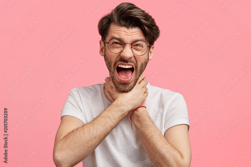 Depressed annoyed male being thick and tired of work, makes suicide gesture, keeps hands on neck, exclaims furiously, expresses negative emotions and feelings. Desperate overworked hipster guy Depressed annoyed male being thick and tired of work, makes suicide gesture, keeps hands on neck, exclaims furiously, expresses negative emotions and feelings. Desperate overworked hipster guy