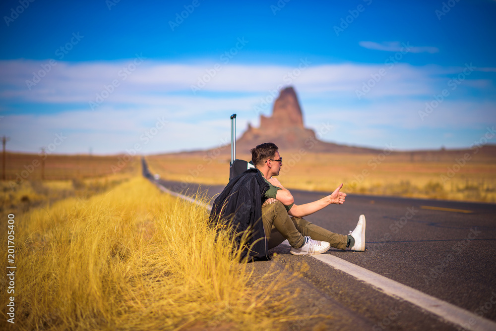 Tired hitch-hiker with suitcase sitting on a road